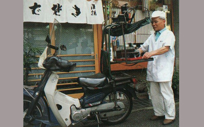 And now,Demae delivery service is practiced with motorbike equipped with the Demae device(1).  ((1)The Demae device is a special rack equipped on the back of a motorbike which swings and rocks on hinges to keep the food safe during transport.)